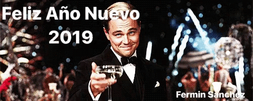 a man in a tuxedo holds a glass of champagne in front of a sign that says " feliz ano nuevo 2019 "
