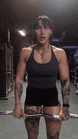 a woman with tattoos is lifting a barbell in a gym .