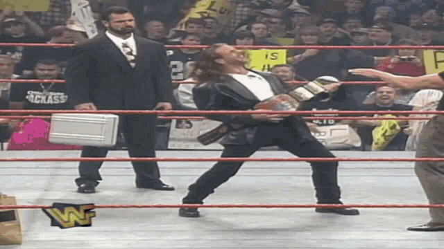 a man in a tuxedo holds a briefcase in a wrestling ring with a wwe logo on the ropes