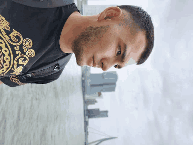 a man wearing a black shirt with a gold design on it looks down
