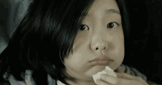 a young girl is holding a napkin in her mouth and making a face .