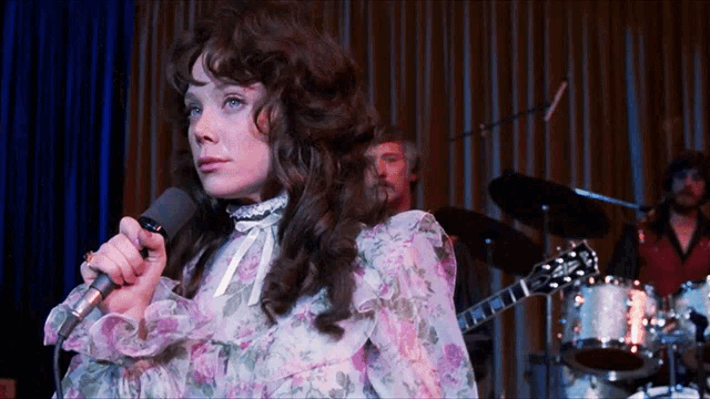 a woman singing into a microphone in front of a drum set