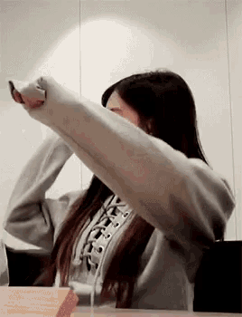 a woman is sitting at a table with her arms outstretched and covering her face with her hands .
