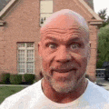 a bald man with a beard and mustache is standing in front of a brick house .