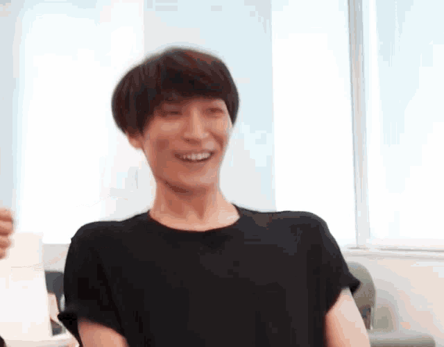 a man in a black t-shirt is smiling in a room .