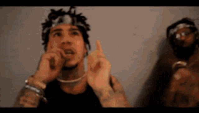a man with dreadlocks is giving the middle finger while another man stands behind him .