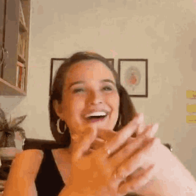 a woman is smiling and clapping her hands while sitting in a room .