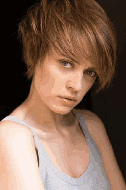 a woman with short hair is wearing a grey tank top and looking at the camera