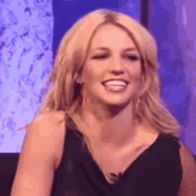 britney spears is smiling and laughing while sitting in front of a television .