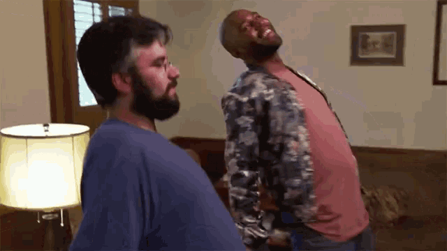 a man with a beard is standing next to another man in a living room