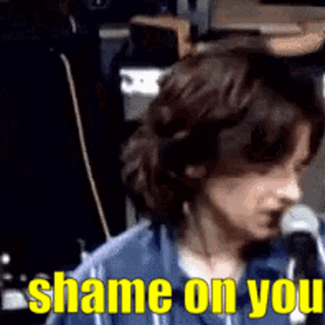 a woman sitting in front of a microphone with the words " shame on you " in yellow letters