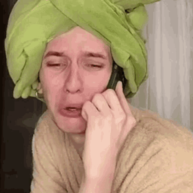 a man wearing a green towel on his head is talking on a cell phone .