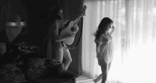a black and white photo of a man playing a guitar and a woman dancing .