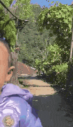 a baby in a purple jacket is walking down a dirt path .