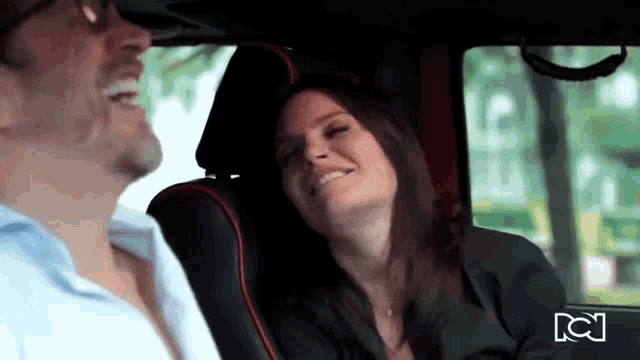 a man and a woman are sitting in the back seat of a car and laughing .