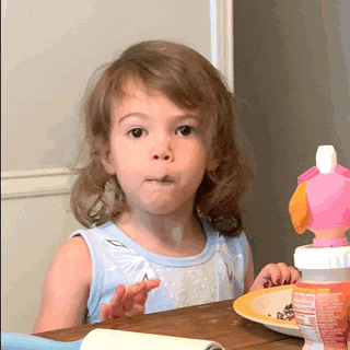 a little girl sitting at a table with her mouth open