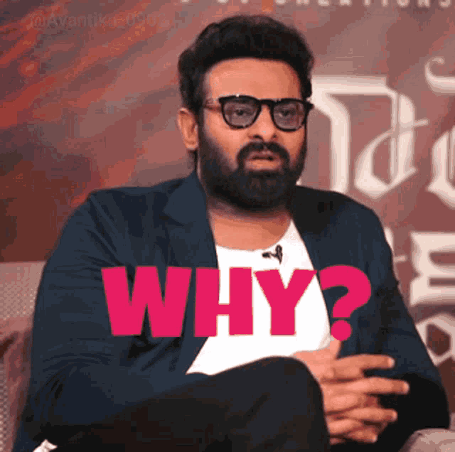 a man with a beard and glasses is sitting on a couch and says why