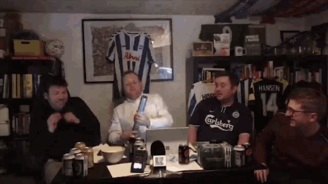 a group of men are sitting around a table with a carlsberg shirt on