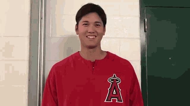a young man wearing a red shirt with the letter a on it is standing in front of a door .