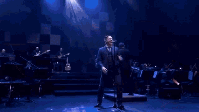 a man in a suit sings into a microphone on a stage
