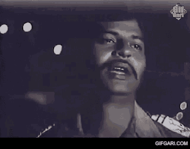 a man with a mustache is talking to someone in a black and white photo .