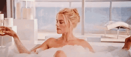 a woman is taking a bath in a bathtub while holding a glass of champagne .