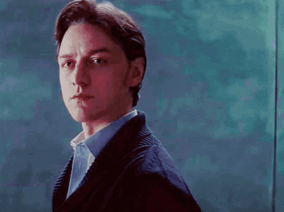 a man wearing a sweater and a blue shirt looks at the camera
