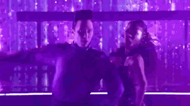 a man and a woman are dancing together on a stage in a purple light .