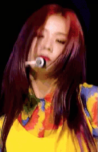 a woman with red hair is singing into a microphone while wearing a yellow shirt .