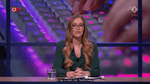 a woman is sitting at a desk in front of a keyboard and says ik leg nu even min telefoonweg