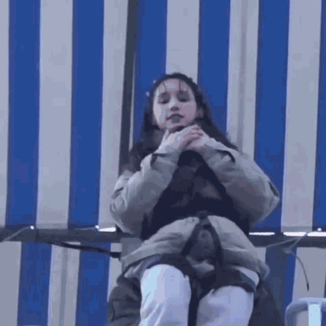 a woman wearing a harness is sitting on a chair in front of a blue and white striped awning .