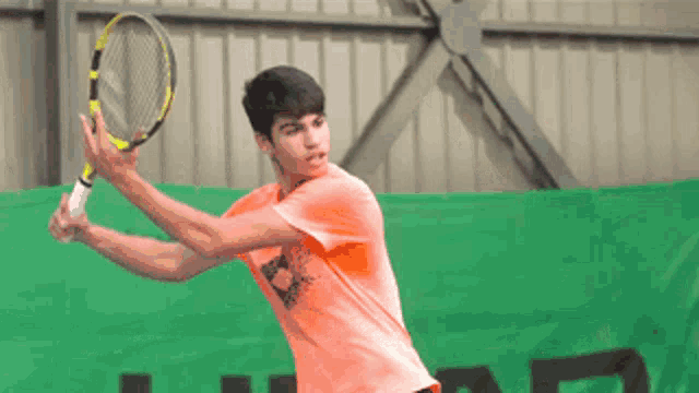 a young man in an orange shirt is swinging a tennis racquet on a tennis court .