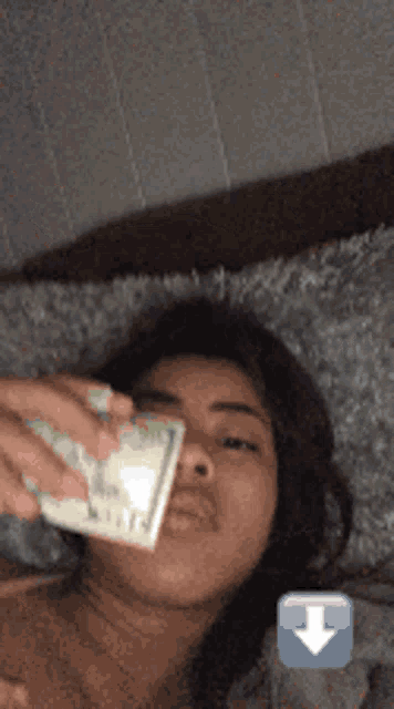 a woman laying on a bed holding a stack of money in her mouth