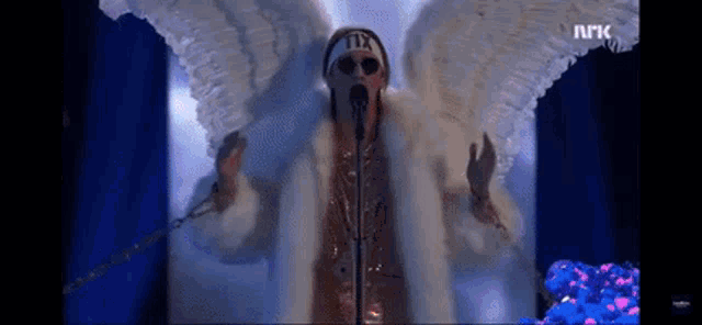 a woman in a fur coat with wings singing into a microphone