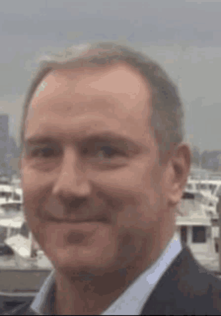 a man in a suit and blue shirt is smiling in front of boats in a harbor .