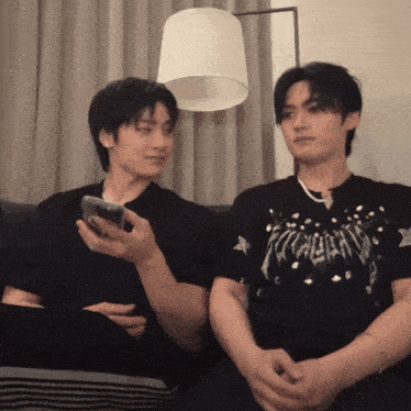 two men are sitting on a couch and one is holding a phone