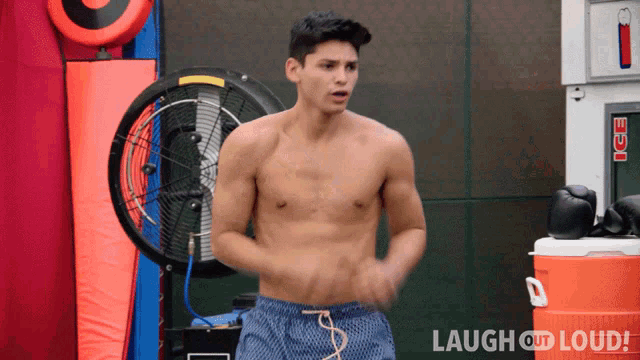 a shirtless man stands in front of an ice machine and a fan