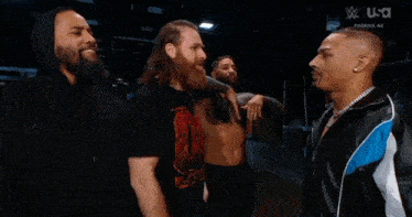 a group of men are standing next to each other in a dark room and one of them is wearing a chain around his neck .
