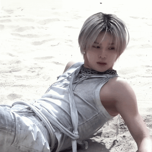 a man in a white tank top laying on the sand