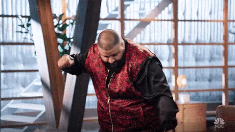 a man in a red jacket is dancing in front of a window in a room .