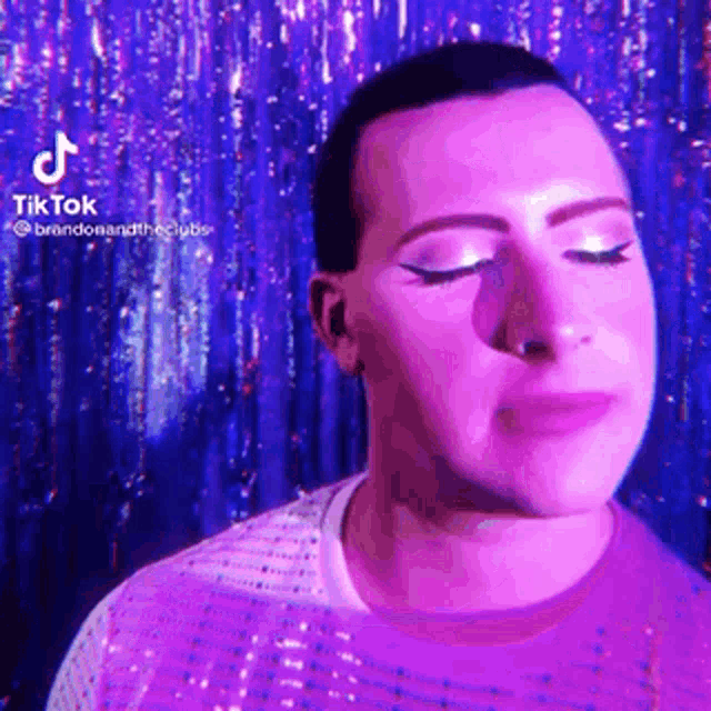 a man in a purple shirt with his eyes closed is standing in front of a purple background .