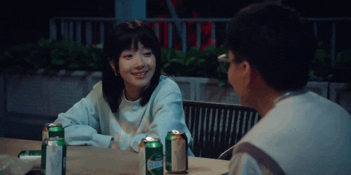 a man and a girl are sitting at a table with cans of beer .