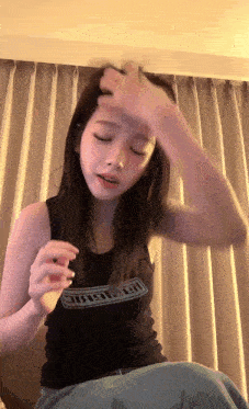 a woman wearing a black tank top with the word magic on it adjusts her hair .