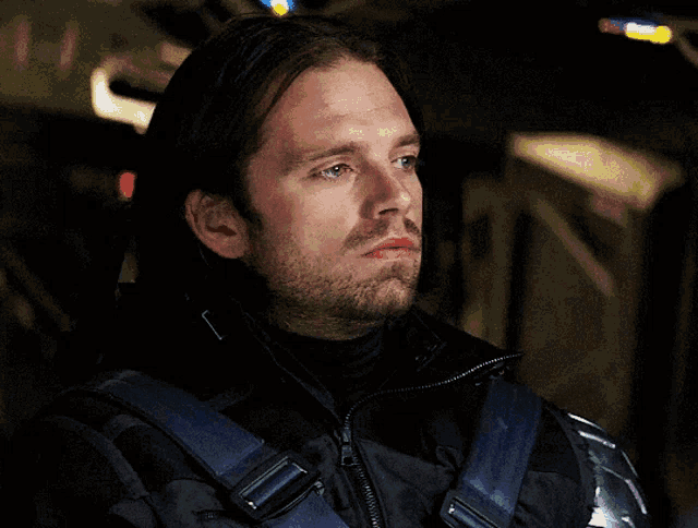 a man with a beard wearing a black jacket with a blue strap around his shoulder