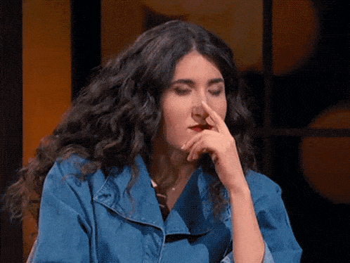 a woman with curly hair is covering her nose with her finger