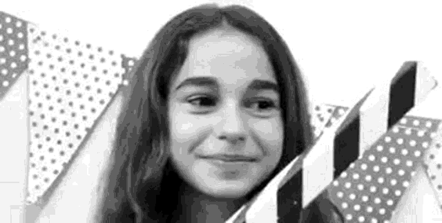a black and white photo of a young girl smiling in front of a polka dot background .