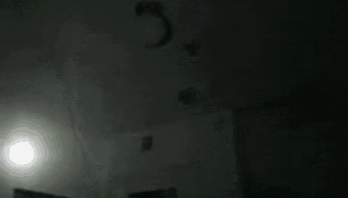 a black and white photo of a person standing in a dark room with a light behind them .