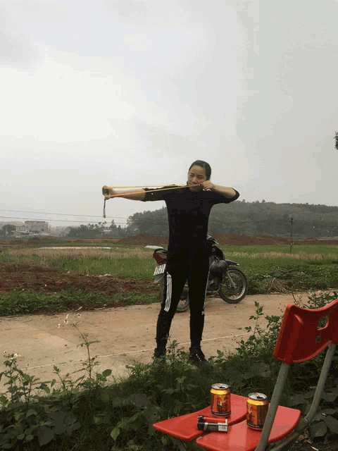 a man is holding a slingshot in front of a field with a motorcycle in the background and a can of coca cola