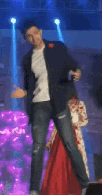 a man in a white shirt and black jacket is dancing on a stage with a superman logo in the background