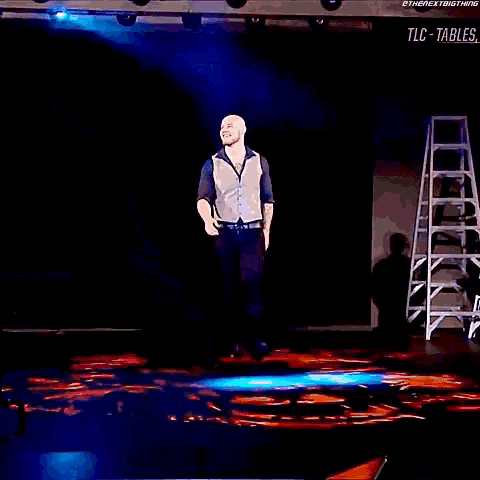 a man is standing on a stage with a ladder in the background and a sign that says tlc-tables on it
